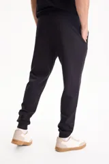 Pantalón de jogging negro sin friza, con puños elastizados en los tobillos y cordón ajustable en la cintura.