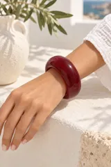 Brazalete rígido de resina en color borgoña, de diseño ancho, liso y brillante.