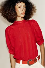 Blusa blanca de cuello alto con detalles de puntilla, manga corta abullonada y cierre posterior con botón.