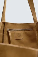 Bolso tipo shopper de piel con acabado serraje color camel, con dos asas de mano y bolsillo interior con cierre de cremallera.