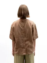 Remera de lino con corte holgado, cuello redondo y mangas cortas. Presenta un diseño minimalista con detalle de botones en la espalda.