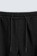 Pantalón tipo jogger de corte slim fit, confeccionado en tejido de algodón con elasticidad. Presenta cintura elástica ajustable con cordón, bolsillos frontales, bolsillos traseros de vivo y bajos con puños elásticos.