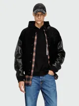 Campera estilo varsity de Diesel, con cuerpo de lana negro y mangas de cuero negro. Presenta cierre frontal con botones a presión, cuello redondo y puños acanalados.