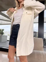 Camisa color crema de corte amplio, con cuello clásico, cierre frontal con botones a presión, mangas largas con puños abotonados y bolsillos de parche en el pecho.