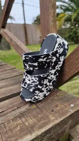 Sandalias de plataforma con doble tira ancha de cuero con pelo natural y estampado animal print de vaca en blanco y negro, con plantilla y suela negra.