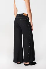 Pantalón de pierna ancha con acabado brillante, confeccionado en lino. Presenta un diseño de tiro medio con cierre de botón y cremallera, bolsillos traseros y etiqueta de marca en la cintura.