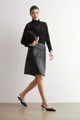 Falda de corte recto y largo midi, confeccionada en eco cuero negro con acabado mate y costuras verticales visibles.