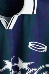 Camiseta de fútbol de manga corta en malla estampada, con diseño a rayas verticales en tonos azul y verde oscuro. Cuenta con cuello polo blanco y escote en V con ribete negro, además de estampados gráficos frontales con estrellas y la inscripción "Run Wild". Presenta un corte holgado.