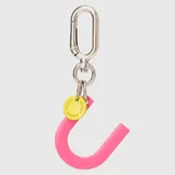Llavero con dije en forma de letra A color rosado y pequeño dije circular amarillo con logo de la marca grabado. Incluye gancho metálico tipo mosquetón.