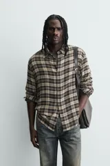 Camisa de corte relajado con diseño de cuadros en tonos negro y beige, cuello camisero, manga larga y cierre frontal de botones.