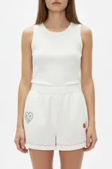 Short ancho de tiro alto confeccionado en mezcla de lino y viscosa, de color blanco. Presenta detalles bordados de un corazón y frutillas en la parte frontal, además de una línea ondulada decorativa en contraste en el ruedo. Cuenta con cintura elástica.