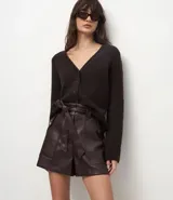 Short de tiro alto confeccionado en poliuretano con acabado que imita el cuero. Presenta cintura elástica con lazo ajustable, bolsillos laterales funcionales y corte recto estructurado.