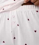 Short de pijama de poliéster color rosado con estampado de pequeños corazones oscuros, cintura elastizada con botones frontales decorativos y terminación de encaje en los bajos.