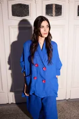 Blazer holgado de lino color azul, con solapas, hombros caídos, bolsillos laterales y cuatro botones grandes de color fucsia en la parte frontal.