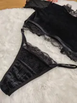 Conjunto de lencería compuesto por un top de cuello alto y una tanga, confeccionados en terciopelo negro con detalles de encaje y microtul. El top presenta mangas cortas con terminaciones en encaje y el borde inferior decorado con una cinta y encaje. La tanga es regulable y combina la textura del terciopelo con bordes de encaje.