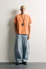 Jeans de denim de algodón color gris con efecto lavado, de corte relaxed barrel fit y tiro medio. Presenta diseño amplio con pinzas en las rodillas y costuras curvas, cierre frontal con botones y cinco bolsillos tradicionales.