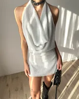Vestido corto de tela brillante plateada con cuello drapeado, diseño halter y espalda descubierta.