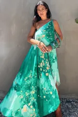 Vestido largo verde con diseño estampado tipo tie-dye y detalles dorados, de corte fluido, un solo hombro y diseño amplio.