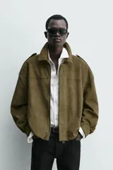 Cazadora cropped fit color verde militar, confeccionada en tejido efecto ante. Cuenta con cuello solapa, manga larga con puño abotonado, trabillas en los hombros, bolsillos laterales ocultos y un bolsillo interior. El bajo tiene elástico interior y el cierre frontal es con cremallera oculta por solapa con botones a presión.