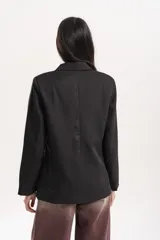 Blazer de corte sastrero en color negro, con diseño de doble botonadura frontal y solapas clásicas. Presenta dos bolsillos laterales con solapa y mangas largas.