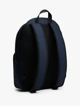 Mochila de poliéster color azul marino con ribetes negros. Presenta un diseño liso, asa superior, correas ajustables y acolchadas, y un panel trasero de malla acolchado. Cuenta con un compartimento principal amplio, funda para portátil incorporada, bolsillo interior con cremallera y bolsillo exterior con cremallera, donde se ubica el logo metálico de Tommy Hilfiger.