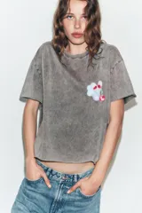 Camiseta oversize de algodón con efecto lavado en color gris, cuello redondo y manga corta. Presenta un estampado gráfico pequeño en el pecho con diseño de nube y cereza.