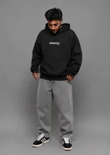 Hoodie canguro negro de algodón pesado con capucha, bolsillo delantero tipo parche y el texto 'NØBASIC CLUB' estampado en blanco en el pecho.
