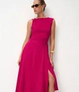 Vestido midi de sastrería color fucsia, sin mangas y con escote redondo. Presenta un adorno metálico dorado en uno de los hombros y una abertura lateral en la falda que aporta movimiento.
