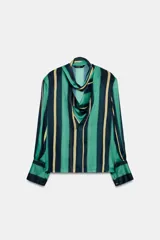 Camisa de manga larga con escote fluido tipo pañuelo, hombreras y puños abotonados. Presenta un diseño de rayas verticales en tonos verdes y amarillos.