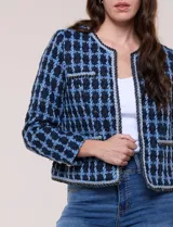 Chaqueta corta de corte estructurado confeccionada en tejido de tweed azul con patrón de cuadros, escote redondo sin solapa, frente abierto, bolsillos falsos y ribetes trenzados con hilos metalizados.