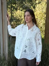 Camisa blanca de broderie con diseño floral, corte oversize, cuello clásico, cierre frontal con botones y mangas largas con puños abotonados.