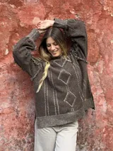 Sweater de punto color marrón con diseño de rombos y líneas verticales en relieve. Presenta cuello alto, mangas largas con detalles de flecos en las costuras y aberturas laterales en el ruedo.