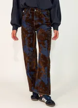 Pantalon de corte recto confeccionado en denim con un diseño estampado de manchas en tonos marrones y azul oscuro. Presenta cierre frontal con botón y bolsillos laterales.