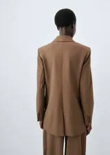 Blazer de corte recto y diseño estructurado, confeccionado en tejido mezcla de lana color marrón. Presenta cierre de doble botonadura, cuello con solapas de muesca, bolsillos de solapa en el frente y bolsillo de ribete en el pecho. Incluye forro interior y mangas largas con puños abotonados.