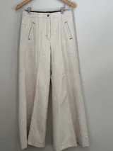 Pantalón de lino y algodón color beige, de tiro medio y piernas anchas. Cuenta con dos bolsillos delanteros y dos traseros con detalles de remaches y atraques.