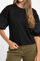 Remera negra de algodón con mangas cortas abullonadas que presentan detalles de encaje bordado y calado en los extremos.