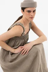 Vestido largo de lino color tostado, con silueta amplia, escote cuadrado con frunces elastizados y breteles anchos con detalles de volados.