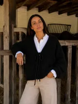 Saco tejido de punto en color negro, confeccionado en lana merino. Presenta un diseño de trama marcada, mangas amplias y cierre frontal mediante un lazo ajustable.