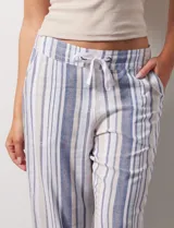 Pantalón capri de lino estampado con rayas verticales en tonos rosa, gris y amarillo. Tiene pretina ancha elastizada, bolsillos inclinados en la parte delantera y cordón ajustable en la cintura.