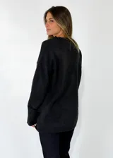 Sweater de punto azul marino con cuello en V, mangas largas con puños acanalados y detalle de línea en color marrón en el cuello y puños. Presenta un pequeño aplique decorativo en la parte inferior.