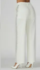 Pantalón sastrero de corte recto y cintura media con elástico en la parte posterior. Presenta una banda lateral decorativa con pedrería brillante a lo largo de ambas piernas, bolsillos laterales y cierre frontal con botón.