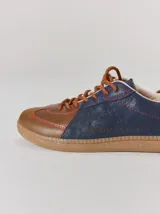 Championes de cuero con diseño tricolor en tonos negro, marrón y crema. Presentan cordones trenzados, costuras a la vista y detalle de pespuntes en el talón.