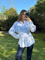 Camisa blanca de silueta entallada con alforzas frontales, cuello clásico, cierre de botones y mangas largas.