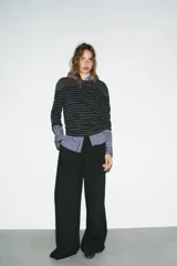 Pantalón de tiro medio con corte recto y holgado. Presenta pinzas en el delantero, trabillas para cinturón y cierre frontal con cremallera, botón y gancho metálico. Incluye bolsillos laterales y detalle de tapetas en la parte trasera.