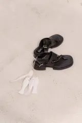 Sandalia de cuero bordó con diseño tipo thong, tiras anchas cruzadas con tachas metálicas doradas, tira con hebilla ajustable en el talón y taco bajo cuadrado con acabado artesanal.