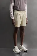 Short de running 2 en 1 color beige, confeccionado en tejido técnico ligero y elástico con malla interior integrada. Presenta cintura elástica ajustable con cordón, bolsillo trasero con cierre y aberturas laterales en el bajo.