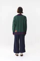 Buzo de tejido de punto con diseño de trenzas, color crema con detalles en marrón en cuello, puños y ruedo. Presenta líneas finas en contraste y pequeñas costuras decorativas en forma de cruz.