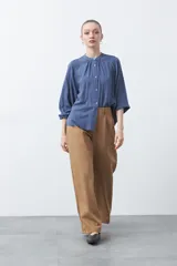 Camisa de color celeste claro con silueta relajada y mangas largas. Presenta un cuello redondo con pequeña abertura frontal y botones, además de un delicado trabajo de tablas en los hombros que aporta textura al diseño.