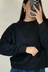 Buzo de cuello redondo y manga larga, color negro, con diseño de pequeños puntos brillantes distribuidos por toda la prenda. Presenta puños y ruedo acanalados.