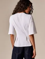 Top blanco de diseño estructurado, con mangas amplias y silueta entallada mediante pinzas frontales. Confeccionado en tela de algodón con caída firme y acabado minimalista.